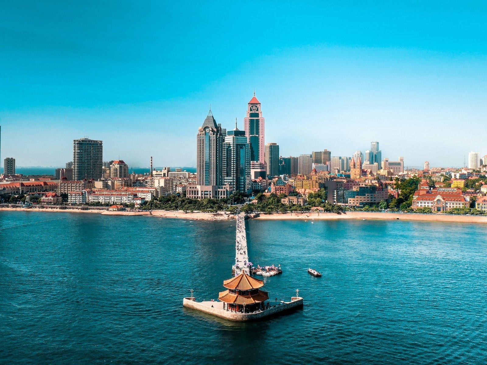 A long pier with a pavilion at its end reaches into turquoise water in front of a beach and high-rise towers