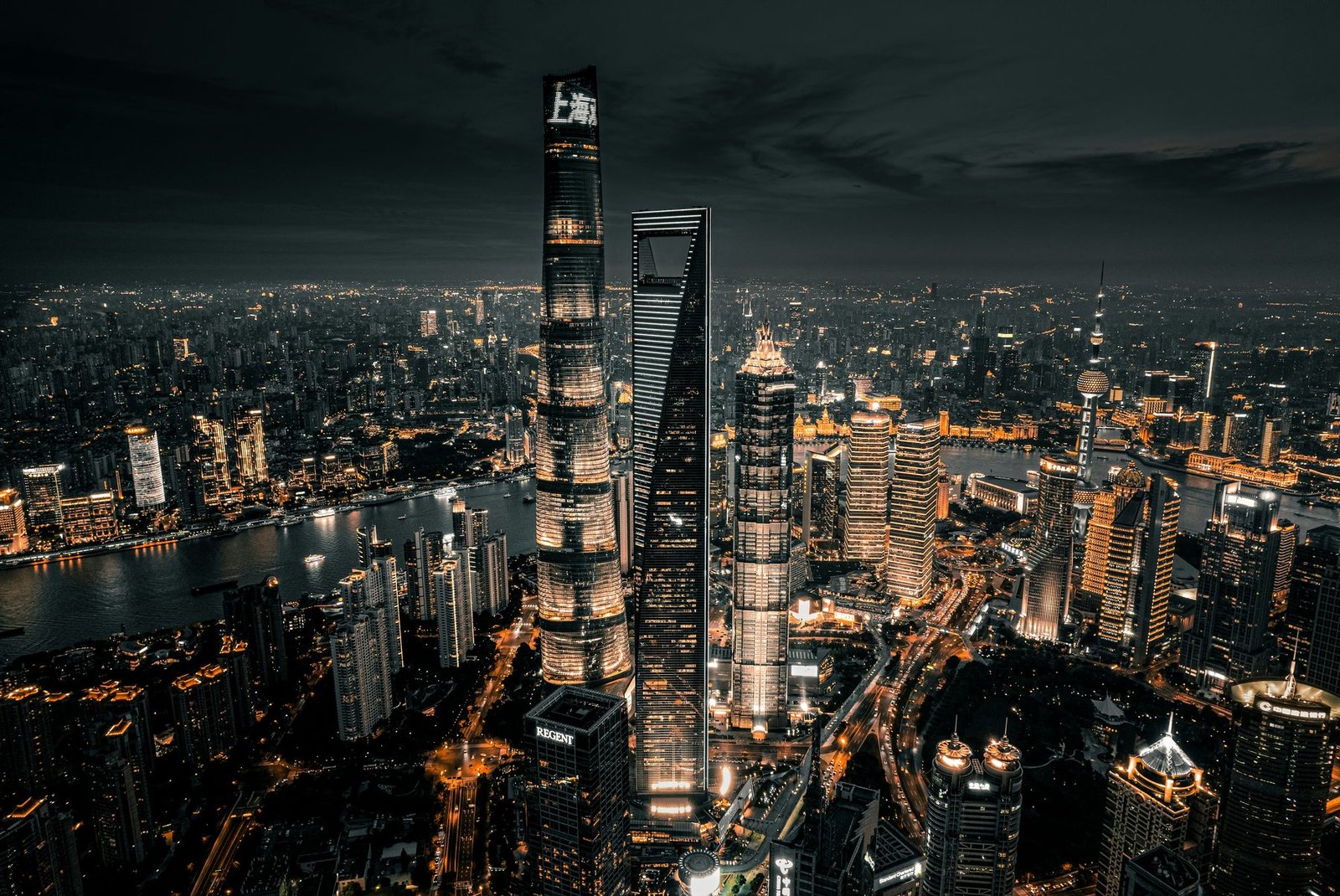 Three very tall towers stand above a city of lights and a curving river