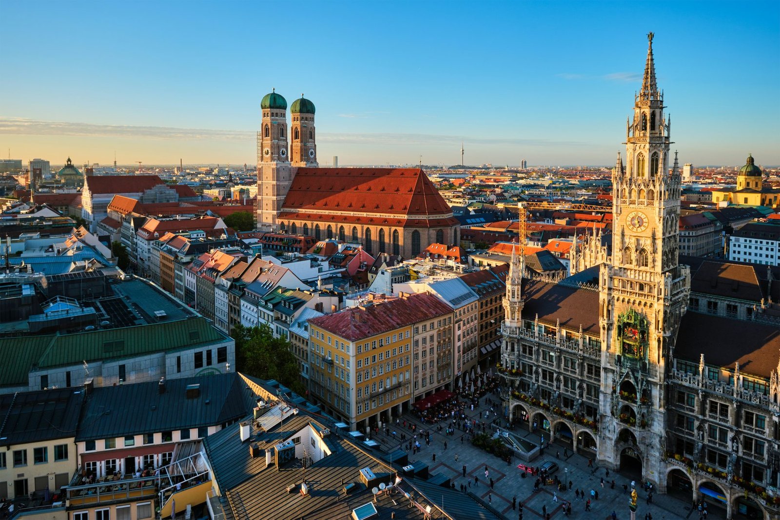 A square seen from above with a neo-Gothic town hall tower on the right and a brick church with two domed towers behind red roofs