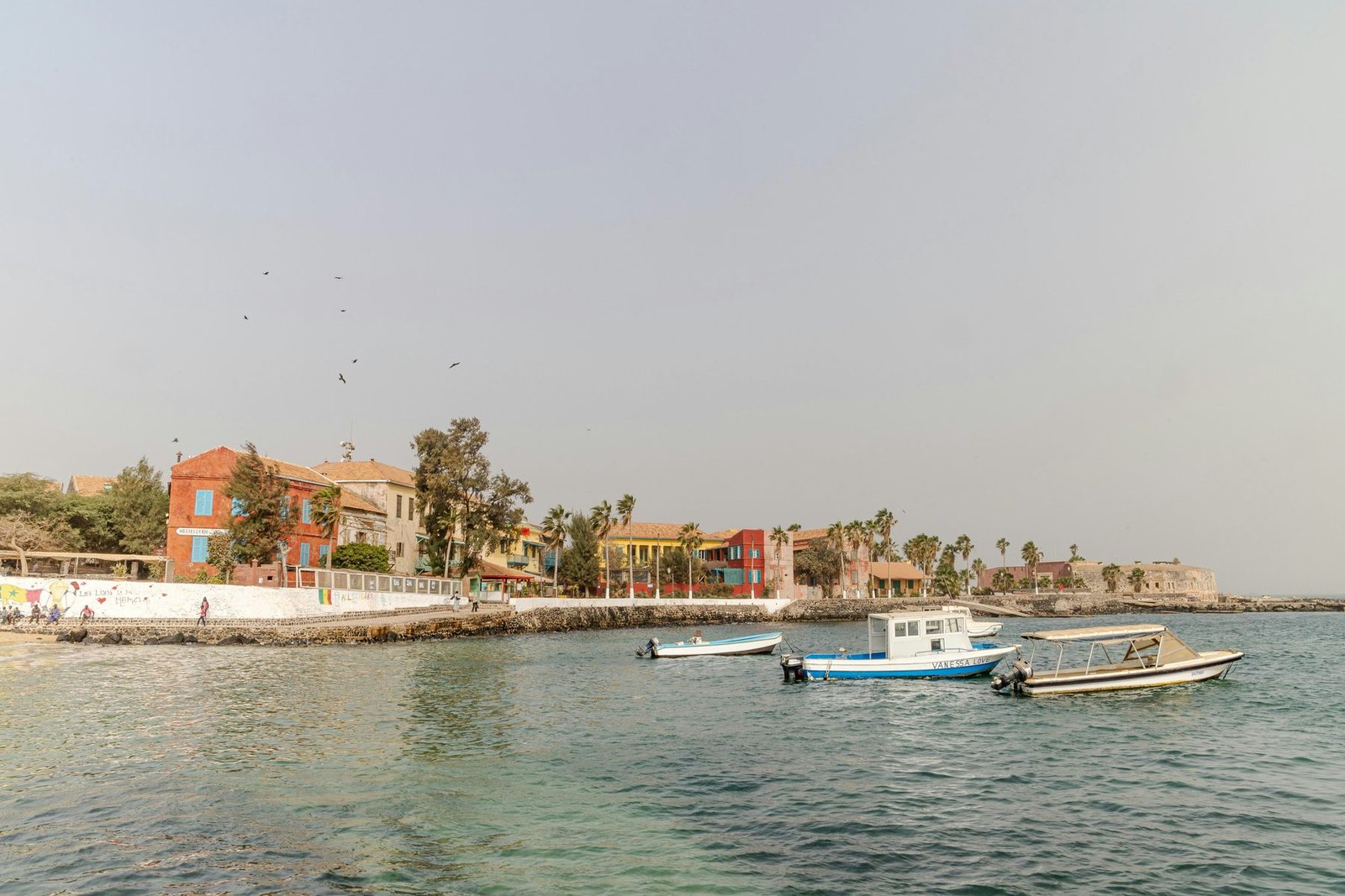 Ocher and red colonial houses and palms line a small harbor with white boats at anchor