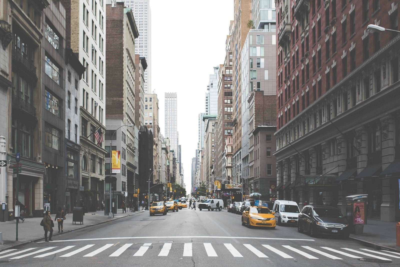A crosswalk and yellow cabs on a quiet avenue