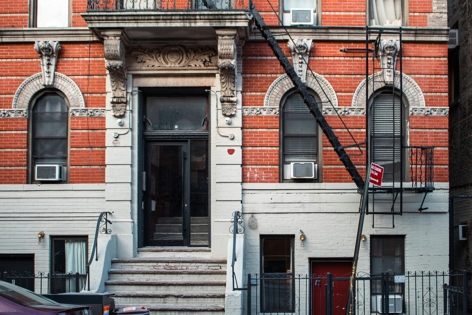 A red-brick tenement front with a fire escape and stoop
