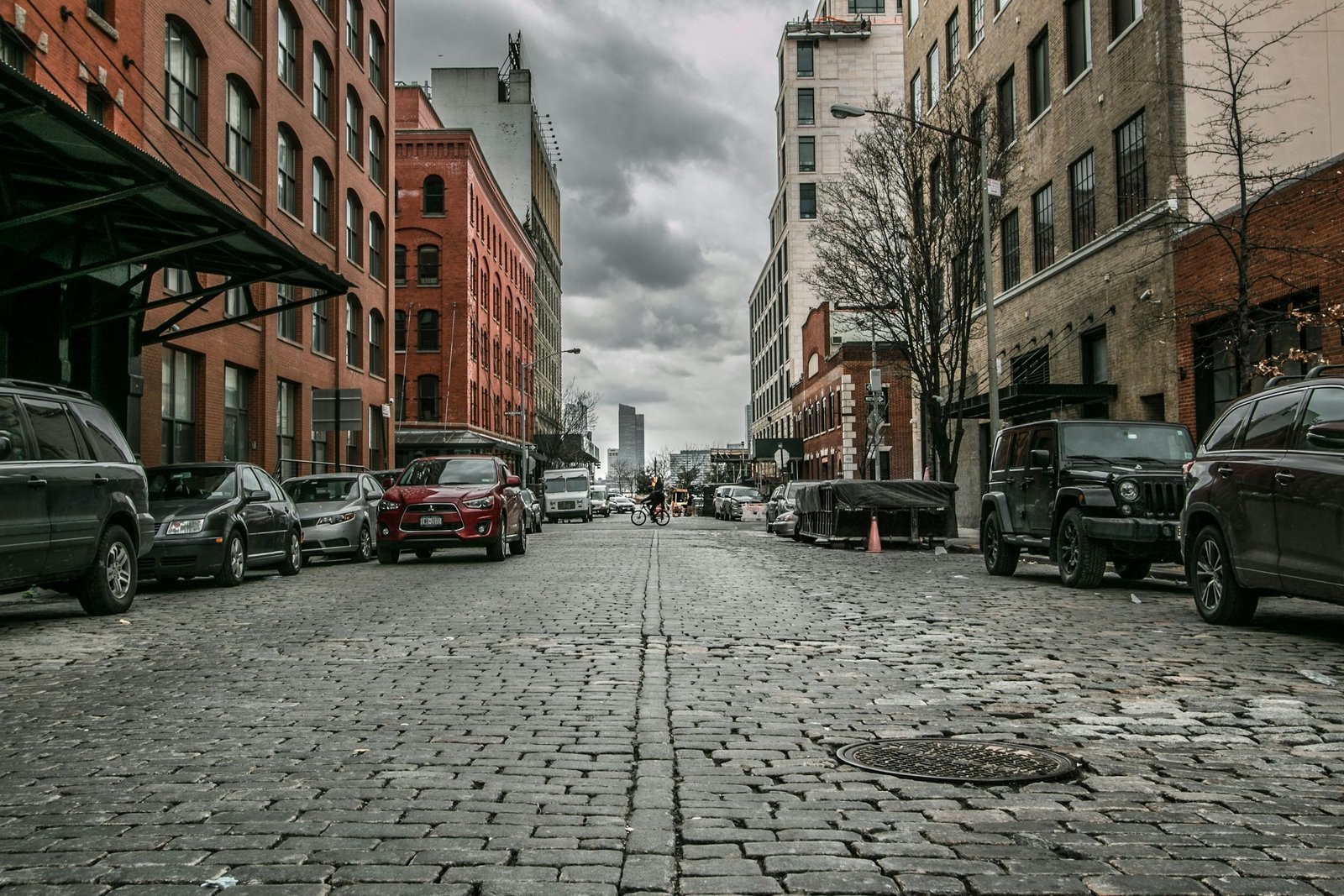 A cobblestone street lined with parked cars and brick buildings